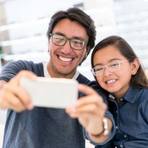 Happy father and daughter buying new glasses at the optician and taking a selfie with her cell phone