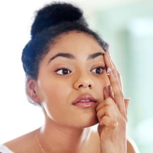 Shot of a young woman putting in contact lenses at home